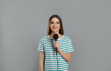 Young female journalist with microphone on grey background