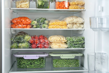 Plastic bags and containers with different frozen vegetables in refrigerator