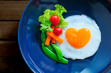 A poached egg heart form served with steamed peas, carrots, cherry tomatoes.