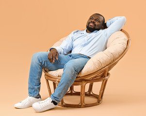 African-American man relaxing in armchair against color background