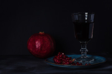 Still life with a whole and open pomegranate and a glass of pomegranate juice on a dark background