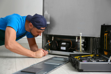 Male technician with screwdriver repairing refrigerator indoors