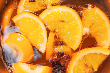 Making hot alcoholic mulled wine with oranges and spices. Christmas beverages boil in the metal pan. Glintwine from rose wine with citrus, cloves, star anise, cinnamon.