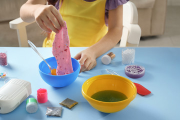 Little girl making slime toy at table indoors, closeup