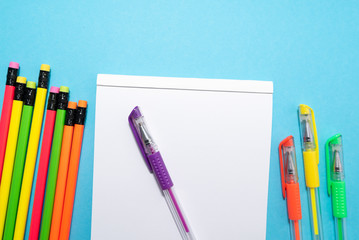 white sheet of notebook, colored pens and pencils on blue background