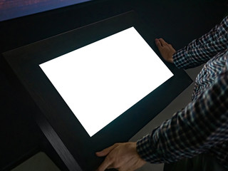 Man looking at white blank interactive touchscreen display of electronic multimedia kiosk in dark room of technology exhibition - close up view. Mock up, copyspace, template and futuristic concept