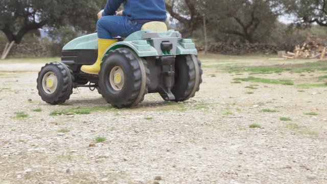 unrecognizable child playing with a toy tractor in the field