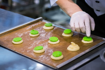 Process of preparing shortbread cookies with bright green filling on kitchen table at cuisine of bakery, restaurant. Professional cooking, catering, bakery, gastronomy and food concept