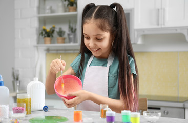 Obraz na płótnie Canvas Cute little girl mixing ingredients with silicone spatula at table in kitchen. DIY slime toy