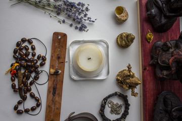 extinct candle, brown rosary, incense, dried lavender flowers and statues of Hindu gods on a white background, top view