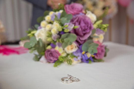 Beautiful toned picture with Engagement rings lie on a wooden surface against the background of a bouquet of flowers . wedding rings and beautiful bouquet as bridal accessories .