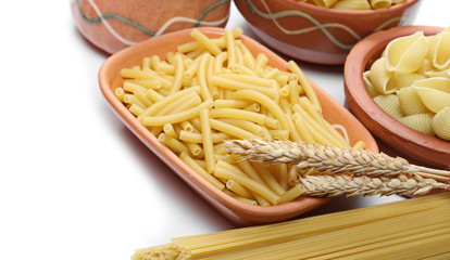 Pasta tubes, dry ears of wheat,   spaghetti, conchiglie grandi, tortiglioni or elicoidali in clay pot, isolated on white background