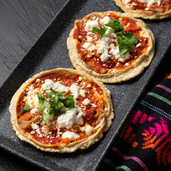 Mexican sopes with red sauce and fresh cheese on dark background