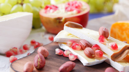 Cheese platter: variety of cheeses on wooden plate with fruits and nuts. Different types of cheese. Camembert, grapes and pomegranate on a classic blue background. Top view