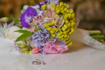 Beautiful toned picture with Engagement rings lie on a wooden surface against the background of a bouquet of flowers . wedding rings and beautiful bouquet as bridal accessories .