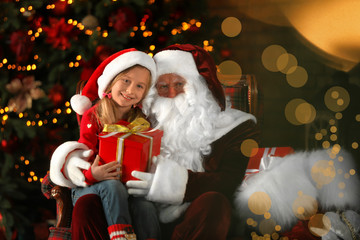 Fototapeta na wymiar Santa Claus and little girl with gift near Christmas tree indoors