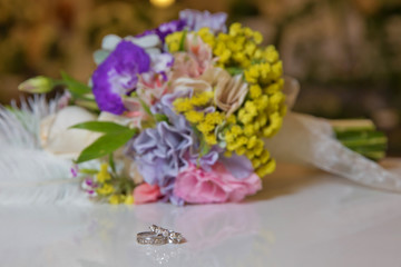 Beautiful toned picture with Engagement rings lie on a wooden surface against the background of a bouquet of flowers . wedding rings and beautiful bouquet as bridal accessories .