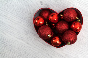 Heart shaped box filled with red christmas toys on wooden background