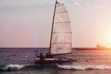 Boat with sail and silhouettes of people in sea water at sunset. Outdoor vacation in mediterranean resort.