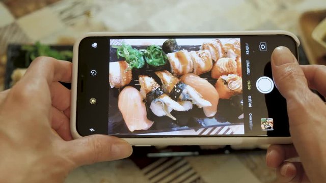 Woman hands taking photos food dinner sushi rolls in a restaurant using a smartphone, a social media addiction concept. Close up. 4K.