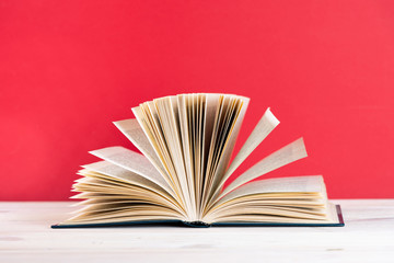 Composition with vintage old hardback book, diary, fanned pages on wooden deck table and red background. Stacking books. Back to school. Copy space. Education