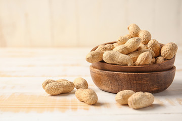Bowls with peanuts on white wooden background
