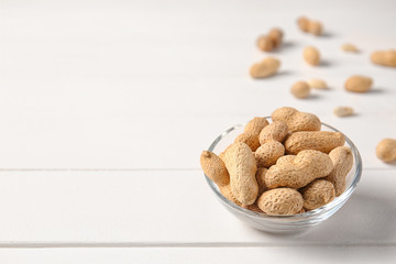 Bowl with peanuts on white wooden background