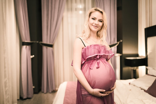 Charming young first-born pregnant woman posing in the bedroom of her luxury home. Concept of healthy pregnant woman expecting firstborn.