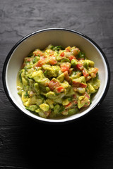 Mexican guacamole with tomato on dark  background