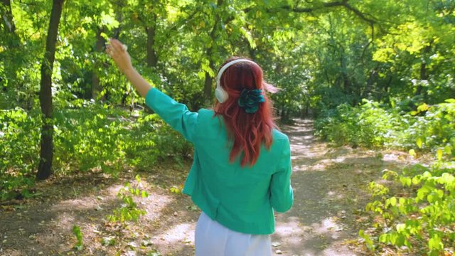 Young happy woman in colorful suit and with pink hair walk in summer park and listen to music