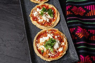 Mexican sopes with red sauce and fresh cheese on dark background