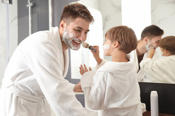 Obraz premium Dad and son with shaving foam on their faces having fun in bathroom