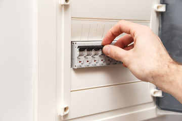 An RCD circuit breaker board with many switches. Man's hand is about switch OFF