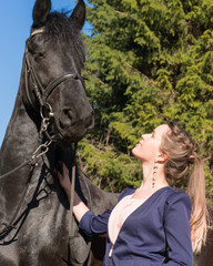Fototapeta premium Woman holds her black horse in forest, outdoors photo.