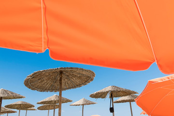 Wicker and textile orange umbrellas on the beach. Blue sky.
