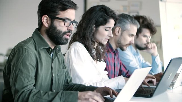 Side view of concentrated programmers working with laptops. Young people sitting in row and typing on laptops. Technology concept