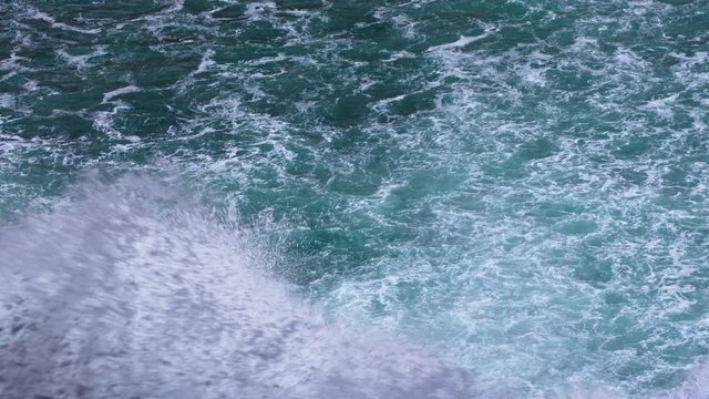 Water waves splashing foam in teal emerald rippled sea. 