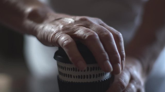 Closeup on barista's hands holding a takeaway cup of coffee or cappuccino and offering it at a customer, at a camera. Woman opening the hot coffee to go disposal with steam.