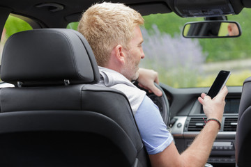 middle-aged man looking at smartphone while driving