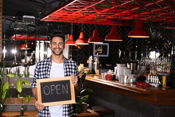 Young business owner holding sign OPEN in his cafe. Space for text
