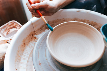 Professional potter works on painting plates in the workshop. Woman paints a ceramic plate with a brush and blue paint