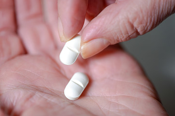 Nahaufnahme: Frau nimmt eine von zwei weißen Tabletten aus ihrer Hand zum Einnehmen - selektiver...