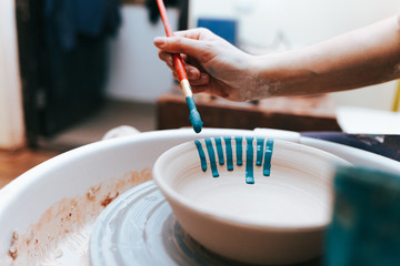 Professional potter works on painting plates in the workshop. Woman paints a ceramic plate with a brush and blue paint