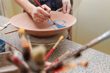 Fototapeta na wymiar Potter woman paints a ceramic plate. Girl draws with a brush on earthenware. Process of creating clay products