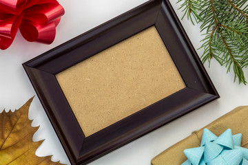 Fototapeta premium Composition Using Empty Picture Frame, Decorative Bow, Pine Branch, Gift Box, and Dry Autumn Leaf on White Background