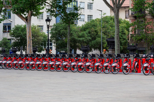 Barcelona, Spain - July 9, 2019: Bright red bicycles available for rent parked in a row at Passeig de Lluis Companys. Concept of environmentally sustainable transport. Bike rental service Bicing.