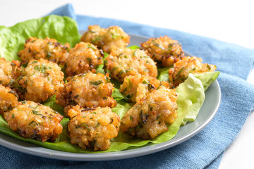 Small fried prawn heaps with garlic and spring onions, finger food or appetizer snack for a festive buffet served on green lettuce leaves on a blue plate and napkin, white table