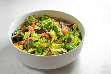 Healthy mixed salad of lettuce, orange, grapefruit, salami and pine nuts in a large bowl, gray to...
