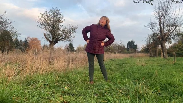 middle-aged woman in a jacket makes bends in the winter or autumn in the park, the concept of becoming slim, athletic and healthy