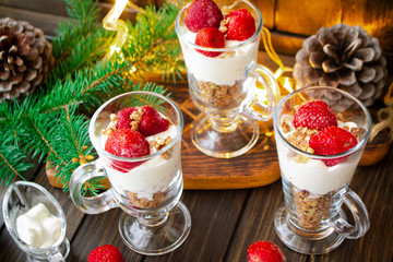 Healthy layered dessert with mousse cream, muesli and fresh strawberry sauce on wooden background with holiday illumination